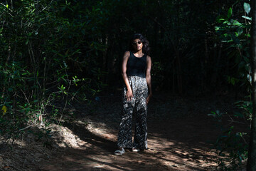 A woman is standing in a forest, wearing black pants and a black tank top