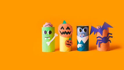 Fototapeta premium Halloween monsters from toilet paper roll tube, easy DIY handmade decorations idea. Paper toys zombie and vampire on yellow background. Kids creativity, easy eco craft, step by step, place for text