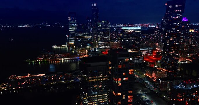 Flight over the luminous waterfront of New York at night. Drone footage over the high-rises of Manhattan and quay.