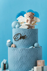 Big two tier birthday cake with blue chocolate frosting decorated with teddy bear flying among the clouds on the plane figurine. Beautiful birthday cake for a little one year old boy. Blue background