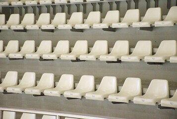 Empty white plastic seats arranged in perfect rows inside a modern sports arena or stadium. Clean and minimal background. Sports events, competition venues, or public gatherings.