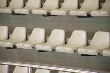 Empty white plastic seats arranged in perfect rows inside a modern sports arena or stadium. Clean and minimal background. Sports events, competition venues, or public gatherings.