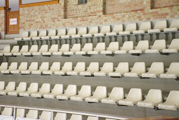 Empty white plastic seats arranged in perfect rows inside a modern sports arena or stadium. Clean and minimal background. Sports events, competition venues, or public gatherings.