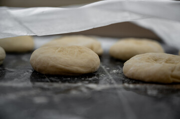 Freshly shaped flatbreads made from raw dough resting under parchment paper during the proofing and resting process.