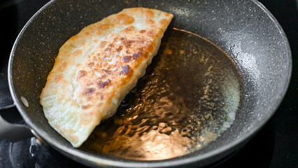 Golden-brown fried cheburek sizzling in a pan. Traditional Eastern European pastry with meat filling, freshly cooked to a crispy texture.