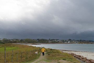 Un homme en ciré jaune qui promène son chien sur la côte en Bretagne