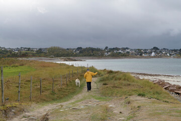Un homme en ciré jaune qui promène son chien sur la côte en Bretagne