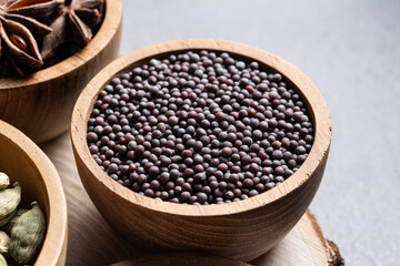 Black mustard seeds in a small wooden bowl close-up on gray surface with warm light. Concept of organic spice and minimalistic culinary style