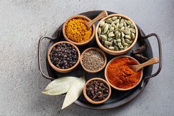 Set of aromatic colorful Indian spices on black metal tray on light gray background, top view. Concept of world flavor and traditional cooking