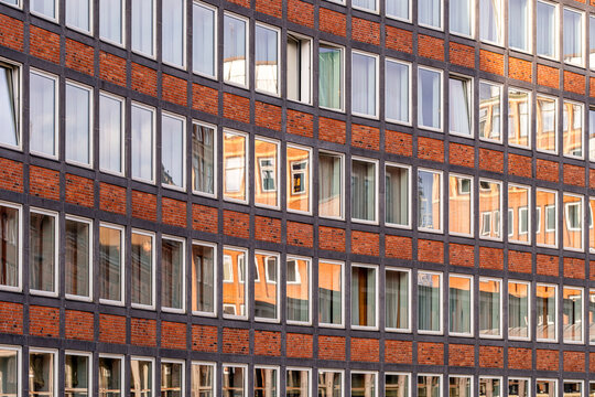 Curved red brick architecture with repetitive windows and geometric rhythm creating dynamic urban facade with warm tones
