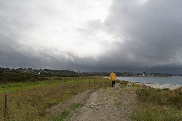 Un homme en ciré jaune qui promène son chien sur la côte en Bretagne