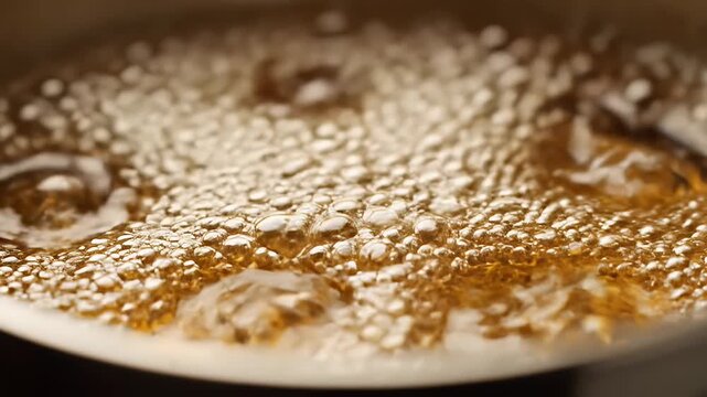Macro shot of hot golden liquid bubbling in a pan.