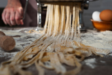 Caucasian female hands making fettuccine noodles using mechanical pasta machine