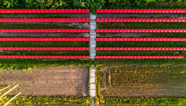 Aerial shot reveals rows of red structures, possibly greenhouses, juxtaposed with green foliage and dirt ground. Cement pathways divide the different areas