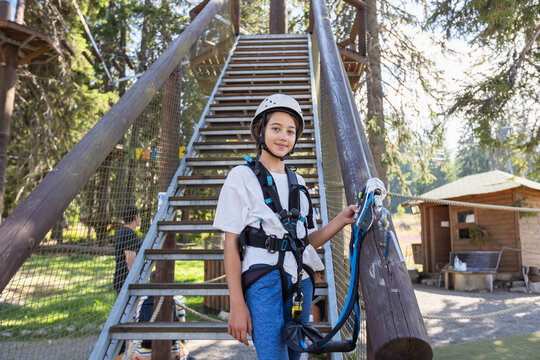 Young girl wearing safety helmet and climbing harness standing confidently at adventure park ropes course. - Powered by Adobe