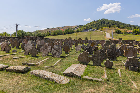 Weathered stone cross gravestones in historic Serbian cemetery at Church of the Holy Apostles Peter and Paul with rural countryside, Novi Pazar, Serbia
