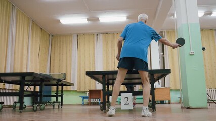 Senior athlete in blue shirt competes in indoor table tennis match against young opponent, showcasing focus, agility, strength, and determination during competitive sports training - Powered by Adobe