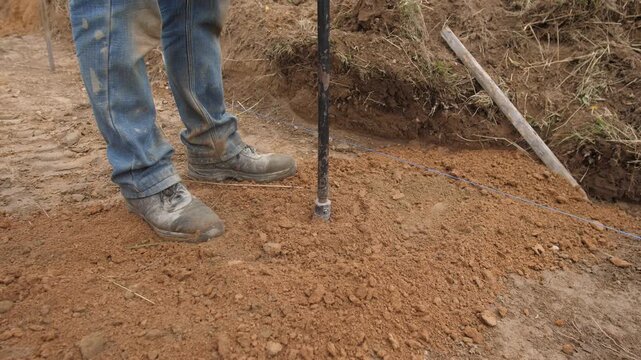 manual soil compaction during construction work, laborer using tamping rod to prepare foundation base, construction worker manually tamping soil to stabilize foundation before setting posts