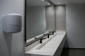 Modern public restroom with black matte faucets, quartz countertop, large wall mirror, and LED...