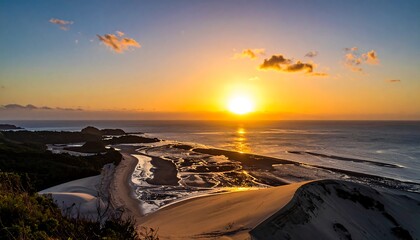An elevated panorama capturing a vibrant sunset over a coastline. The sky is ablaze with colors reflecting on the ocean