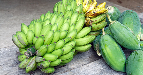 Assorted tropical fruits—green and ripe bananas, fresh papayas—resting on rustic wood, showcasing natural ripeness and farm freshness.
