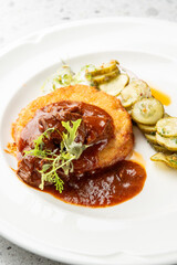 A gourmet meal of traditional potato pancakes with meat goulash and a side of fresh cucumber salad, served on a pristine white plate.