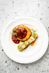 A gourmet meal of traditional potato pancakes with meat goulash and a side of fresh cucumber salad, served on a pristine white plate.