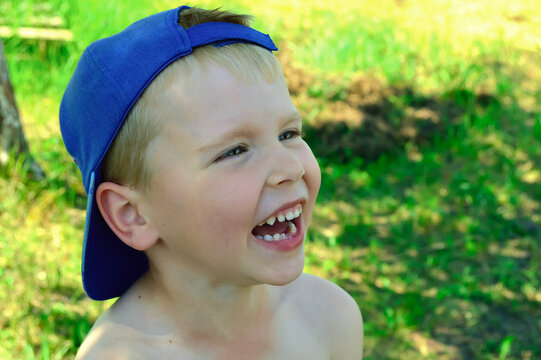 close-up - the boy laughs cheerfully, walking in the garden in the backyard, a blue cap on his head