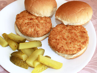 Two crispy breaded chicken burgers placed on buns with a side of dill pickles