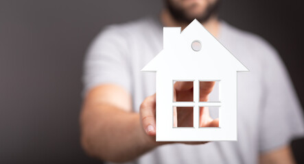 A person holding a white house cutout, symbolizing home ownership, real estate, dreams, investment, and the concept of a new home.