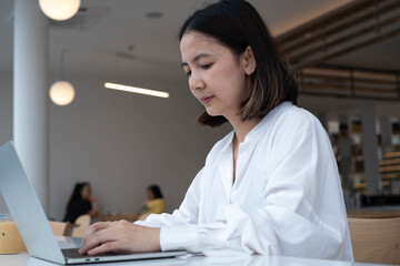 Focused young woman working on laptop in modern cafe, representing remote work, online learning, freelance lifestyle, digital business, and professional communication concepts.