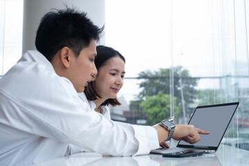 Man and woman discussing work on laptop in modern office near window, symbolizing teamwork, startup collaboration, digital project, online communication, planning, and professional productivity.