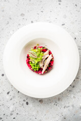 A colorful and delicious Russian vinaigrette salad with beets, potato, peas, and fresh greens, served with herring fillets on a white plate.