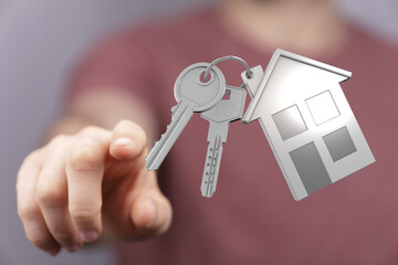 Close-up shot of hand pointing at a keychain with keys and house charm, conveying concepts of homeownership, buying, selling, and investment in