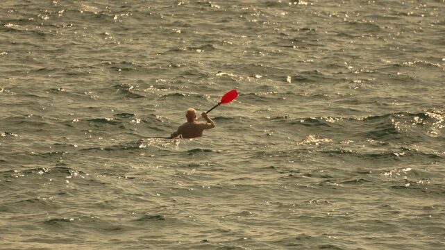 Kayaking ocean water, man paddles orange kayak on calm sea at golden hour.