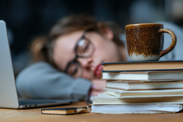 Student taking a nap on books with coffee cup in a cozy study environment during late afternoon
