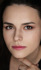 Obraz premium oman with dark, wavy hair and freckles, wearing a black top, touching her forehead while looking to the side in a dark indoor portrait with soft lighting
