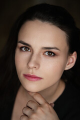 Obraz premium oman with dark, wavy hair and freckles, wearing a black top, touching her forehead while looking to the side in a dark indoor portrait with soft lighting
