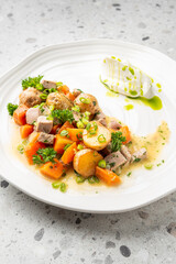 gourmet meal featuring pan-seared meat, roasted potatoes, and carrots, garnished with fresh herbs and a creamy sauce on a modern white plate.