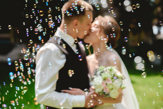 A beautiful wedding photo. The happy newlyweds take a picture in a park with soap bubbles. - Powered by Adobe