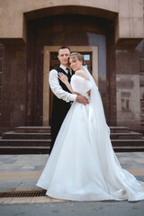 A happy bride and groom, holding hands, stroll through the city on their wedding day. A loving couple, the newlyweds, take photos.
