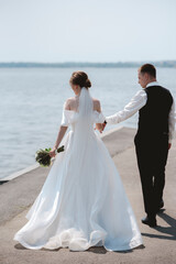 Happy, sensual newlyweds embrace. A happy bride and stylish groom hold hands and stroll through the city.