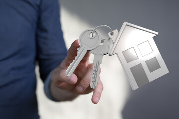 Close-up of hand holding house keys with house shaped keychain. Represents homeownership, real estate, and the dream of owning a house. Perfect