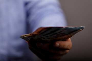 Close up image of hand offering banknotes, representing financial transaction, generosity, or...