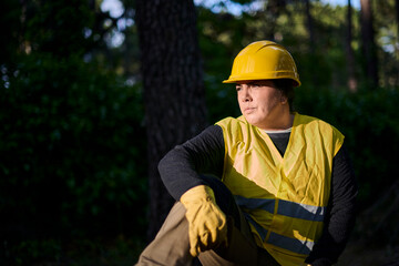 Female lumberjack wearing work clothes rests after finishing her day cutting trees in a forest at...