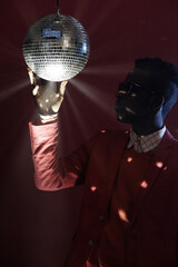 Portrait of fashionable African American guy in sunglasses and suit twisting shiny disco ball while standing in the dark studio
