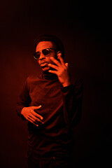 Portrait of stylish Black man in sunglasses rapping and gesticulating while standing in dark room...