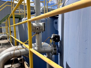 Industrial equipment and piping system featuring valves, sensors, and large blue tanks enclosed by...