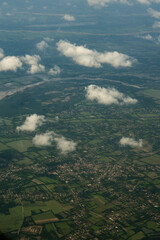 City Landscape Under Thick Clouds from Airplane. Aerial view of a city partially covered by thick white clouds. Airplane view showing vibrant green agricultural fields with small clouds.