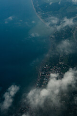 Aerial photograph of a coastal town and shoreline partially covered by white clouds. Beautiful landscape with blue sea, coastline, and urban area seen from above.